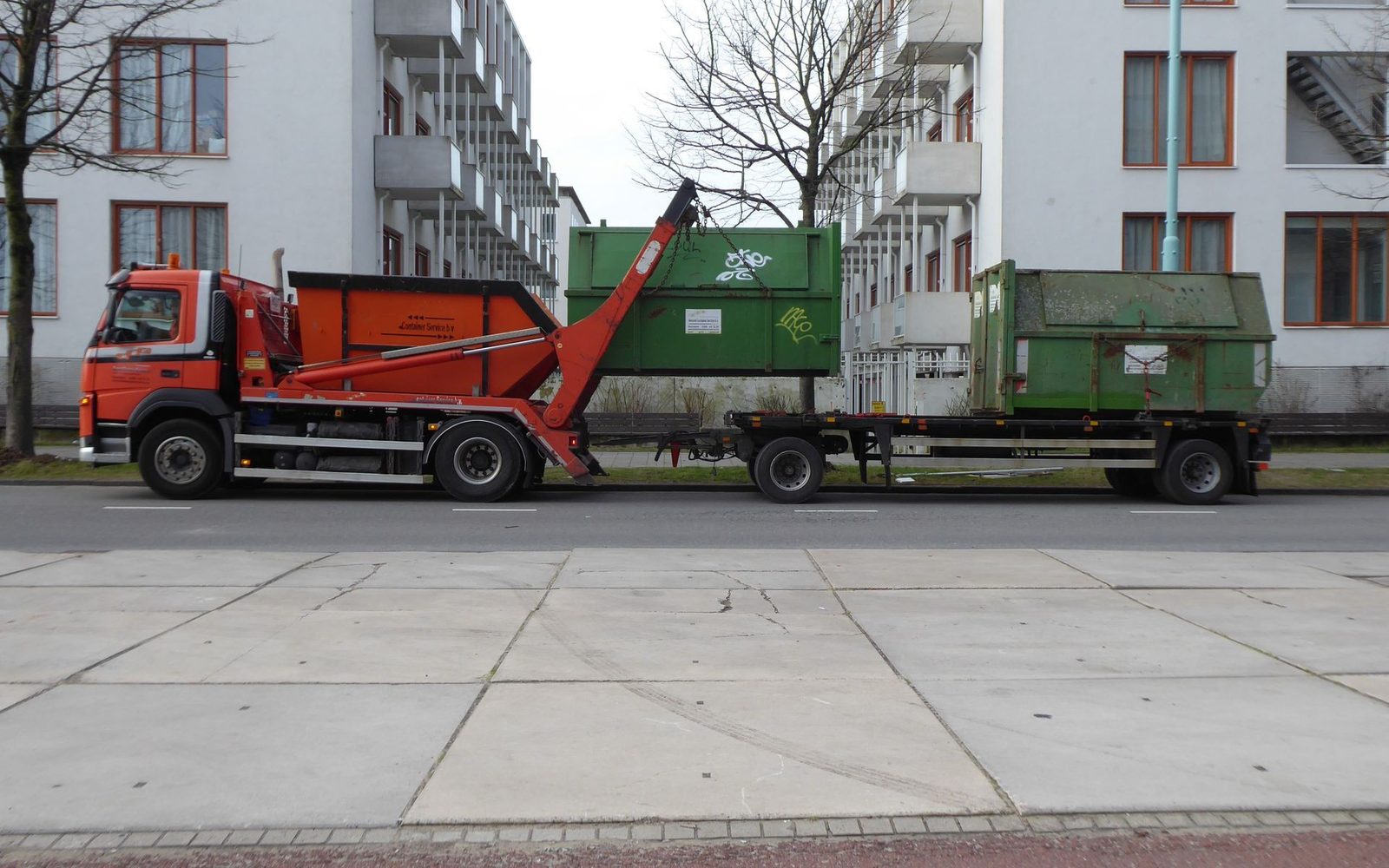 Skip loader lorry lifting a waste container on a residential street